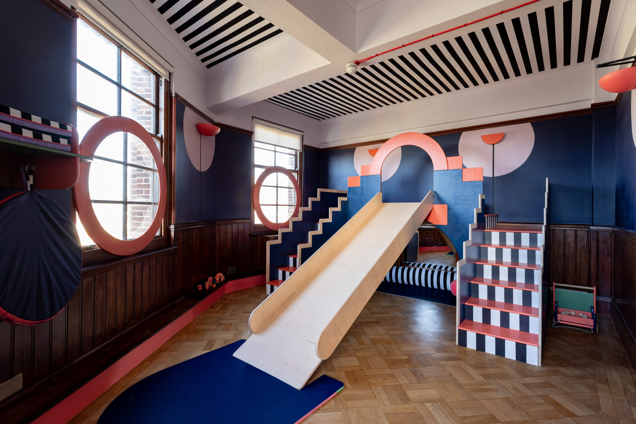 A view of Tiny Tetley Studio, including a slide, stripy ceiling, and stripy steps and circles painted onto the wall