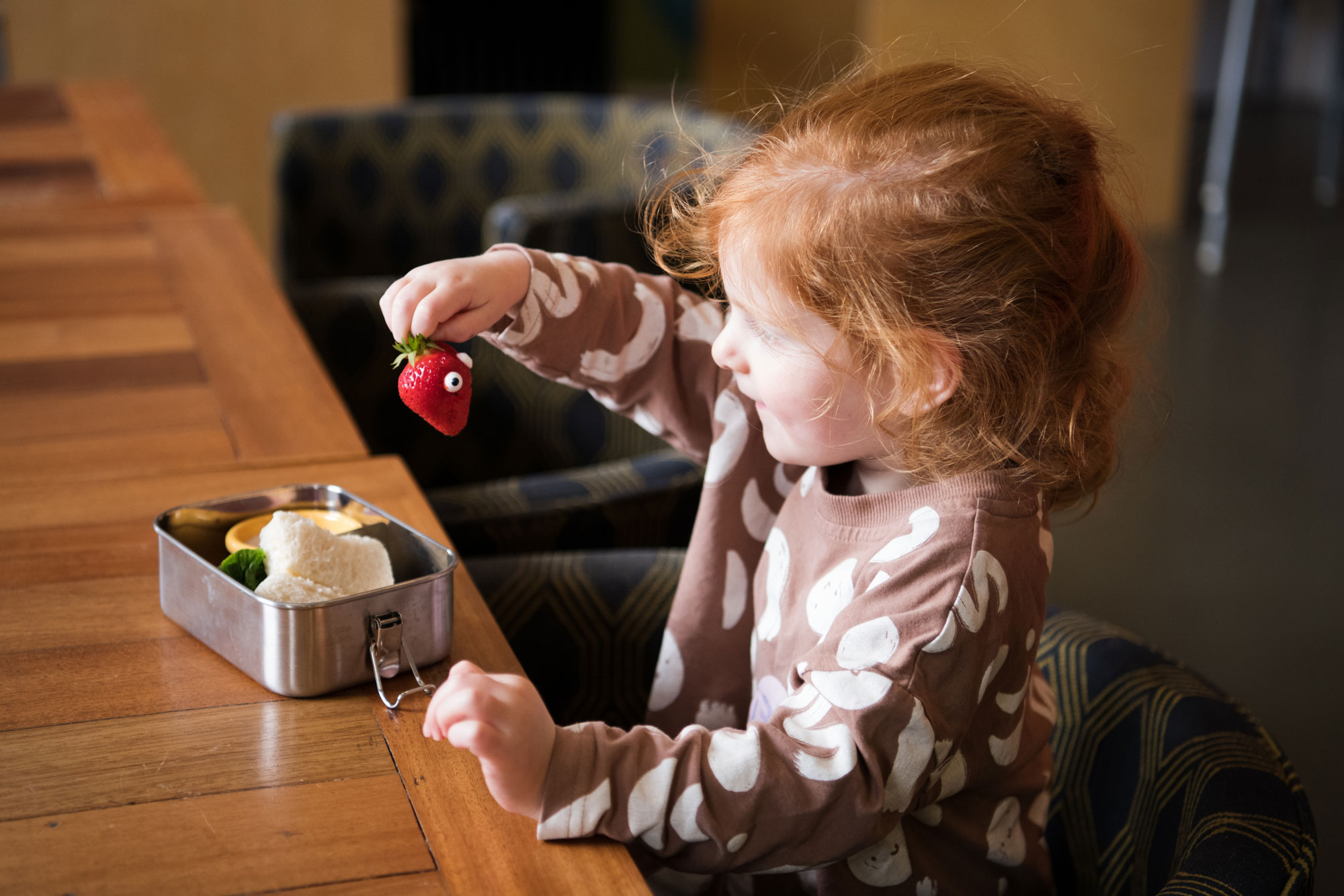 A child smiles and holds up a strawberry